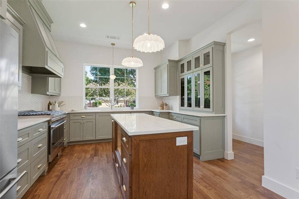 304 S Weatherred Drive, Richardson, TX 75080 Kitchen featuring sage cabinetry, a wood-finish island with quartz countertops, custom glass-front display cabinetry, wood-finish flooring, and pendant lighting