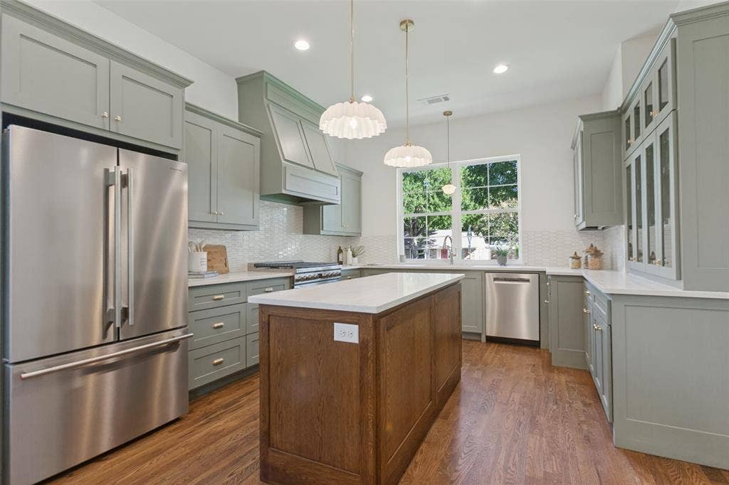 304 S Weatherred Drive, Richardson, TX 75080 Kitchen featuring sage green cabinetry, a center island with a wood finish, light-toned stone-style countertops, stainless steel appliances, and textured tile backsplash