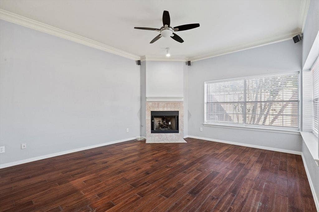 892 Brentwood Drive, Coppell, TX 75019 Living area featuring wood-finish flooring, a corner fireplace with stone-surround tile, crown molding, a multi-blade ceiling fan, and large windows with integrated blinds