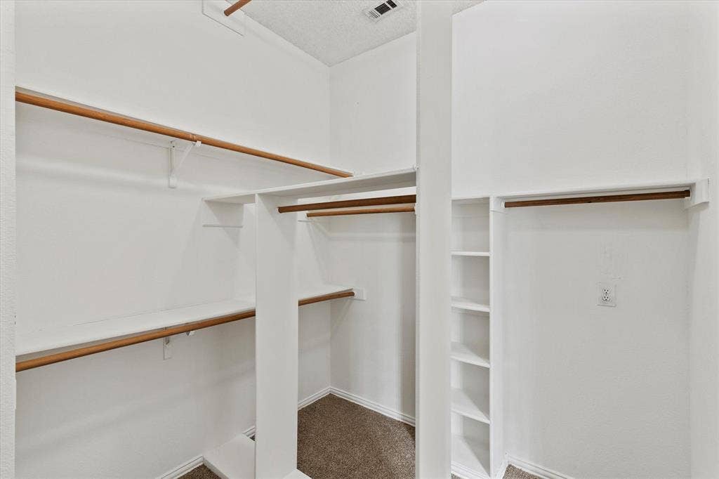 892 Brentwood Drive, Coppell, TX 75019 Walk-in closet featuring multi-level hanging rods, built-in shelving units, and neutral carpeting