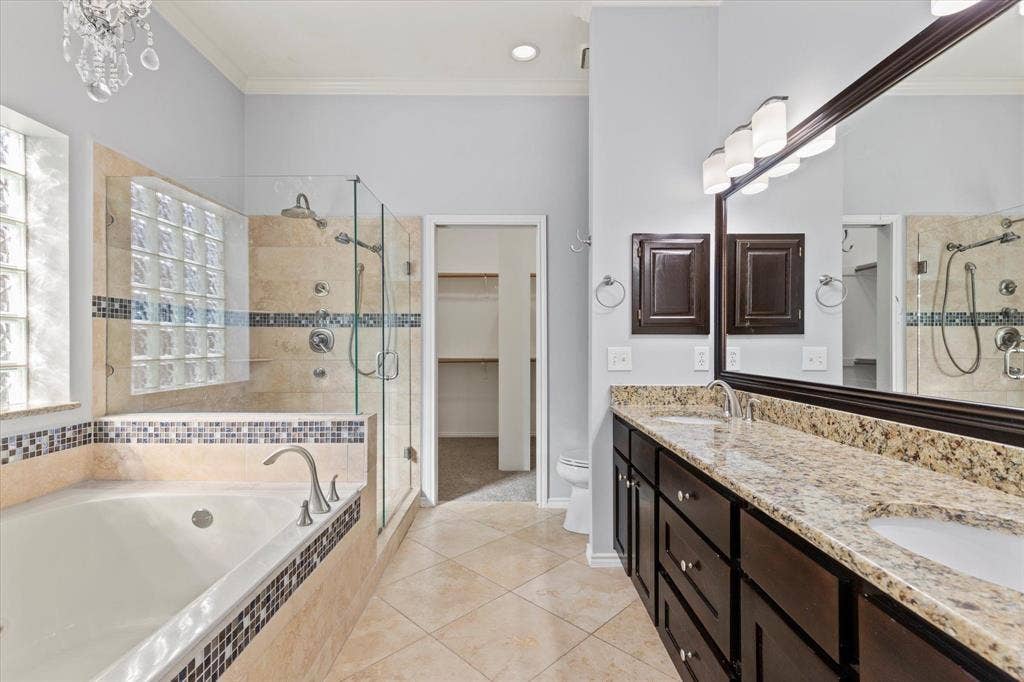 892 Brentwood Drive, Coppell, TX 75019 Bathroom featuring a dual-sink vanity with stone countertops, a deep soaking tub, and a separate glass-enclosed shower with tiled surround