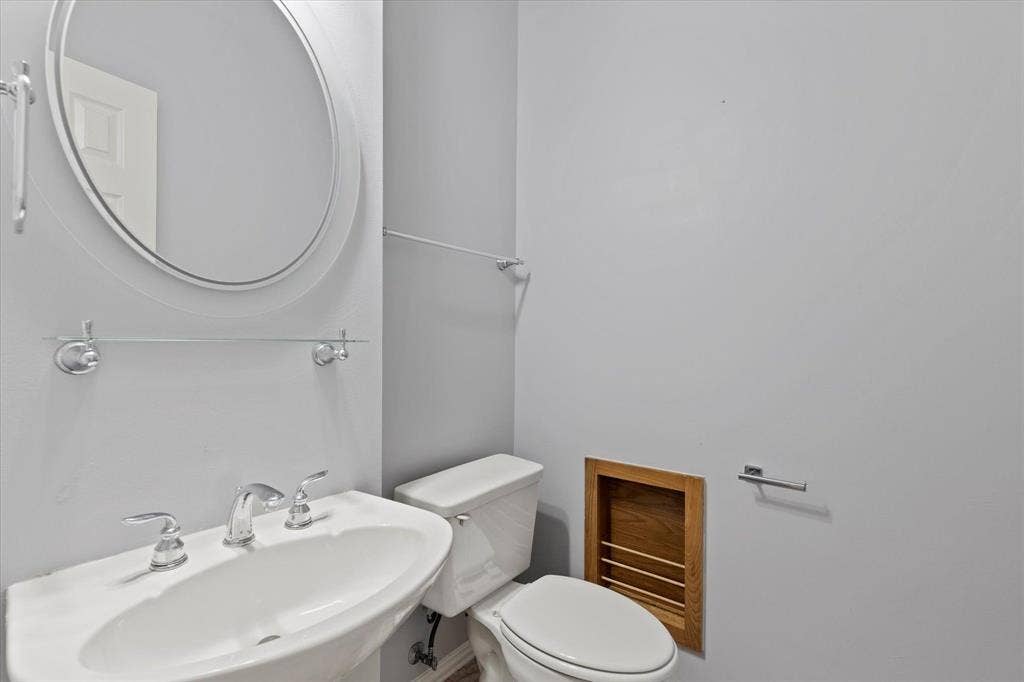 892 Brentwood Drive, Coppell, TX 75019 Guest half-bath with Pedestal sink with chrome widespread faucet, oval wall-mounted mirror, glass shelving, and recessed wood-trim wall niche