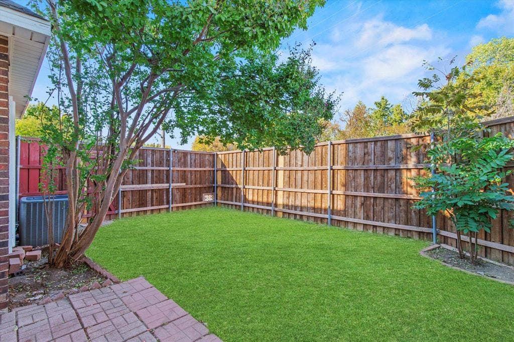 892 Brentwood Drive, Coppell, TX 75019 Fenced backyard featuring a manicured lawn, brick patio, mature trees, and wooden privacy fencing