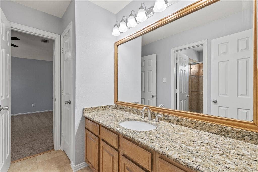 892 Brentwood Drive, Coppell, TX 75019 Upstairs Jack and Jill bathroom. Vanity featuring wood cabinetry, stone-finish countertop, undermount sink, expansive wood-framed mirror, and multi-bulb wall-mounted lighting fixture