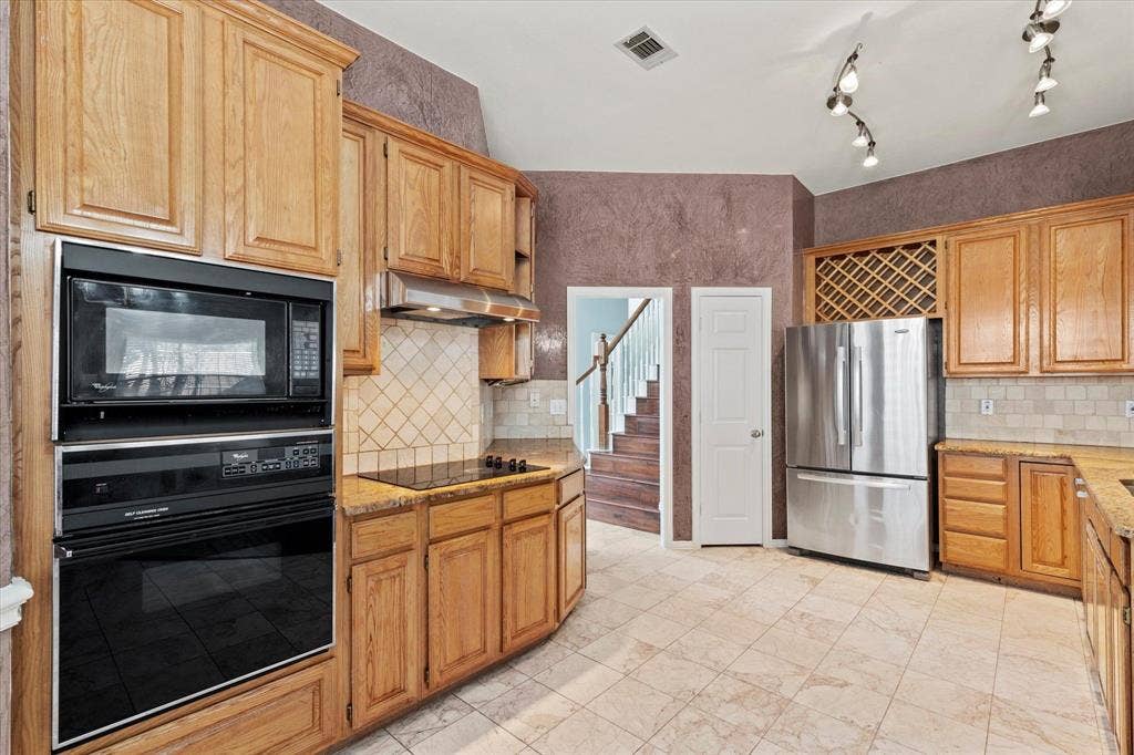 892 Brentwood Drive, Coppell, TX 75019 Kitchen featuring custom wood cabinetry, stainless steel appliances, built-in wine storage, tile flooring, and stone-finish countertops