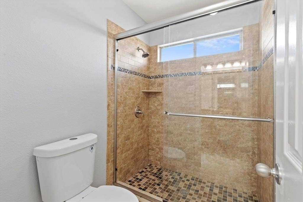 892 Brentwood Drive, Coppell, TX 75019 Upstairs Jack and Jill Bathroom.Walk-in shower featuring a sliding glass enclosure, stone-finish tile surround, decorative mosaic tile inlay, integrated shelving, and a horizontal transom window