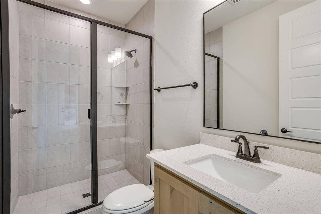501 Olson Road, Waxahachie, TX 75167 Bathroom featuring a walk-in shower with tile surround, glass enclosure, and matte black fixtures, stone-finish countertop with an undermount sink, and a black-framed mirror