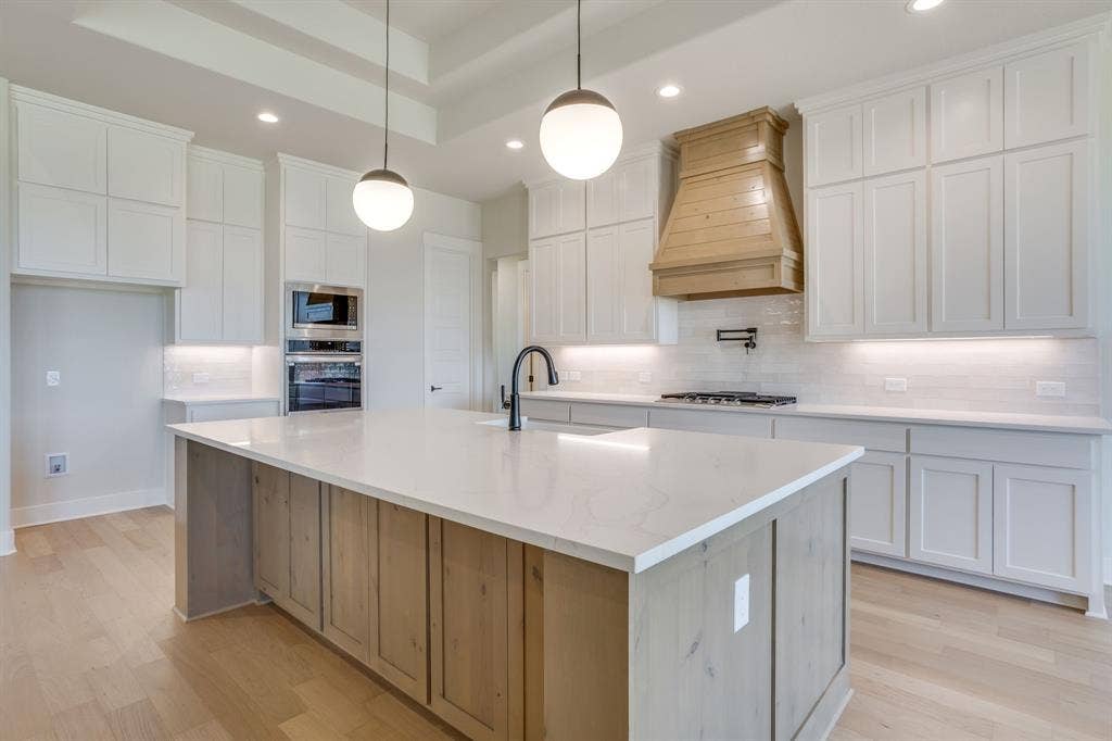 501 Olson Road, Waxahachie, TX 75167 Kitchen featuring white shaker cabinetry, a central island with wood-finish base and light-toned countertop, a custom wood vent hood, globe pendant lighting, and built-in double wall ovens
