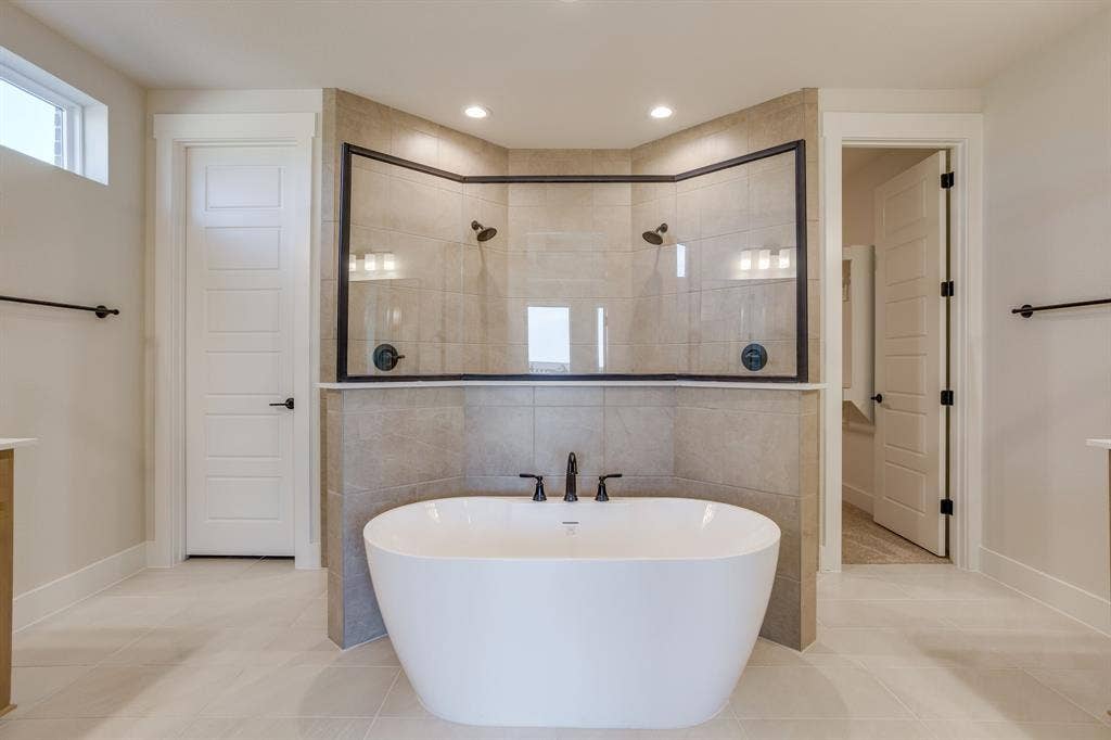 501 Olson Road, Waxahachie, TX 75167 Freestanding soaking tub with a deck-mounted faucet, complemented by an enclosed tile shower featuring dual showerheads, dark metal framing, and a tiled partition wall