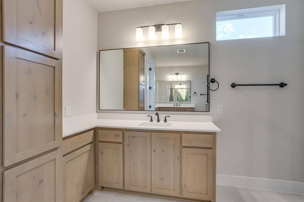 501 Olson Road, Waxahachie, TX 75167 Natural wood-finish cabinetry, quartz countertop with an integrated rectangular sink, large rectangular mirror, matte black fixtures, and transom window