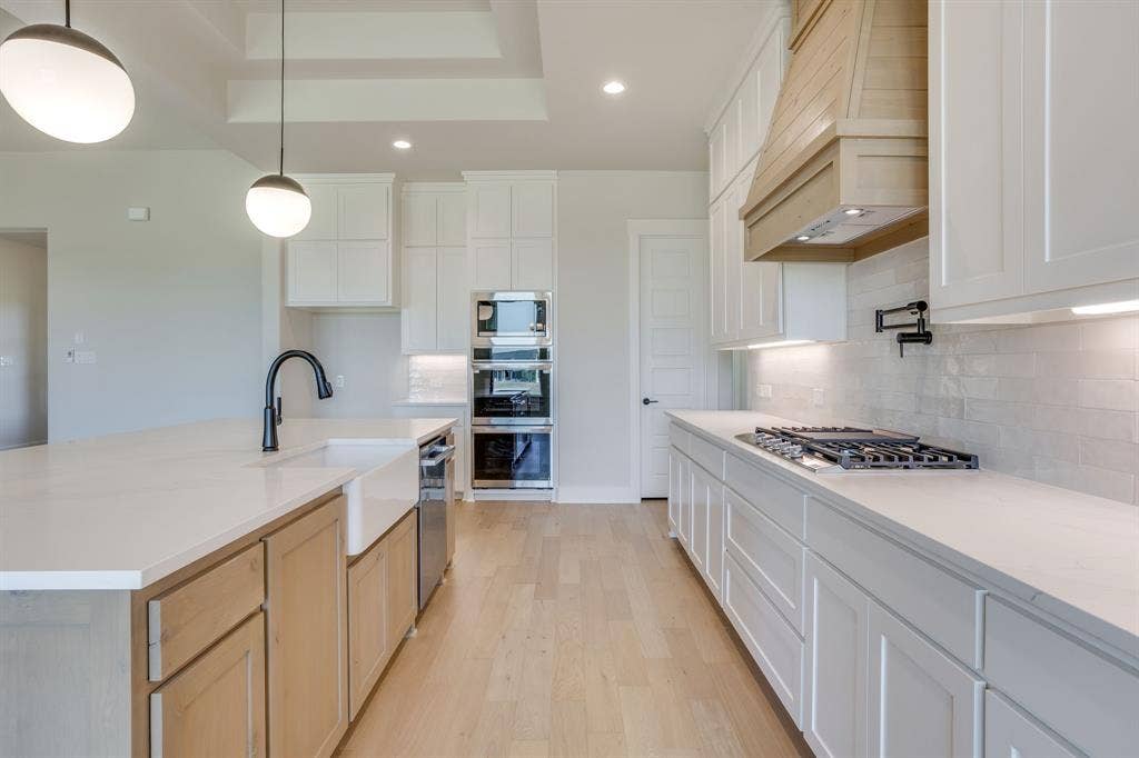 501 Olson Road, Waxahachie, TX 75167 Kitchen featuring white cabinetry, wood-finish island base, quartz countertops, farmhouse sink with matte black faucet, and built-in stainless steel double ovens