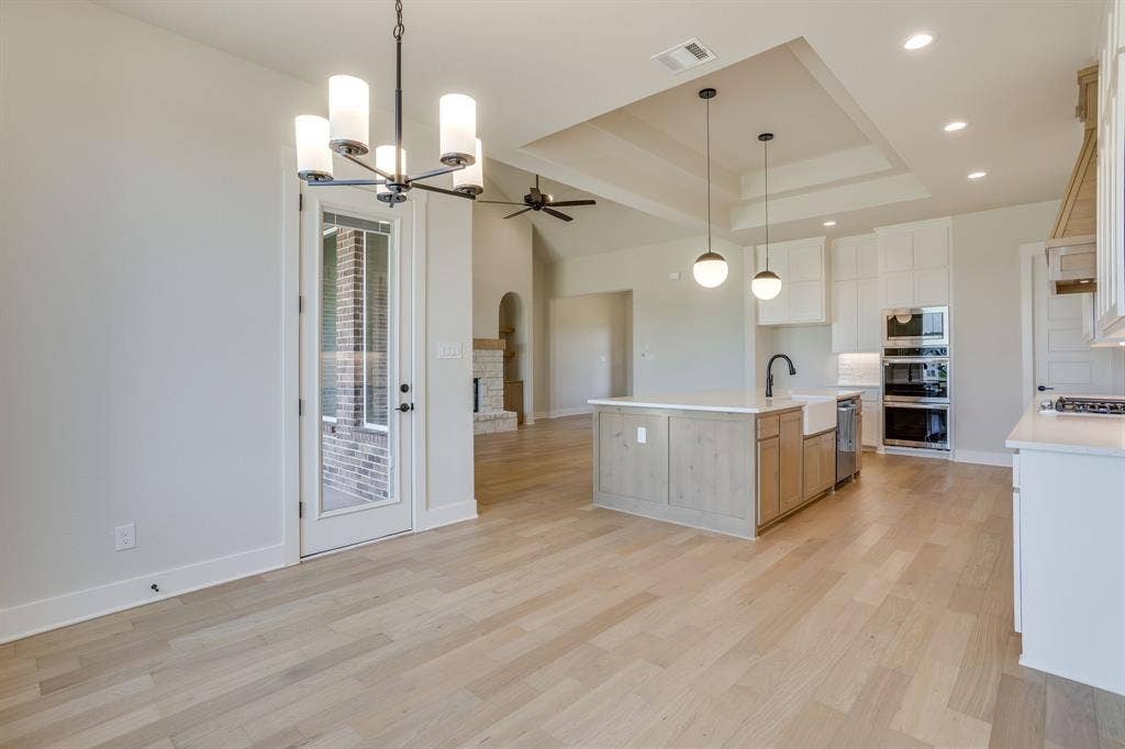 501 Olson Road, Waxahachie, TX 75167 Open-concept kitchen featuring an island with a farmhouse sink, stone countertops, custom cabinetry, stainless steel double wall ovens, and wood-finish flooring