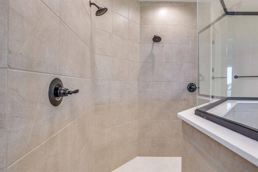 501 Olson Road, Waxahachie, TX 75167 Walk-in shower featuring large-format neutral tile, dual wall-mounted shower heads, dark-finish hardware, and glass enclosure with a solid-surface threshold