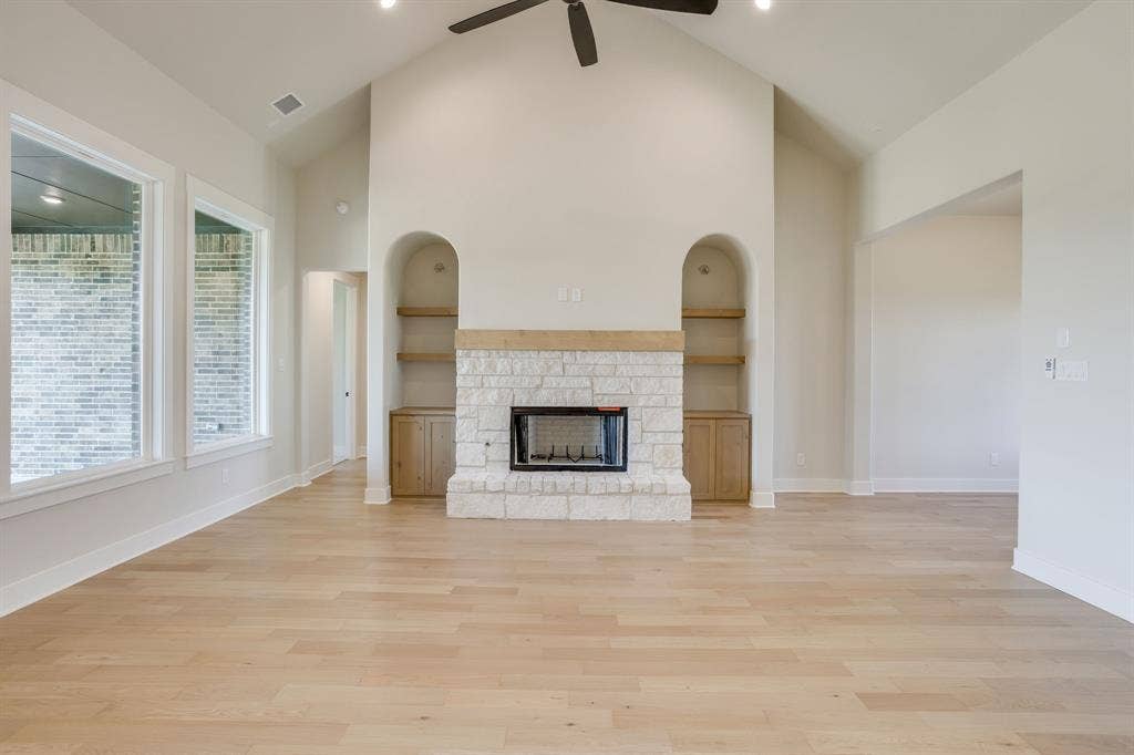 501 Olson Road, Waxahachie, TX 75167 Vaulted ceilings featuring a central fan, light wood-finish flooring, and a floor-to-ceiling stone fireplace surround with a timber mantel