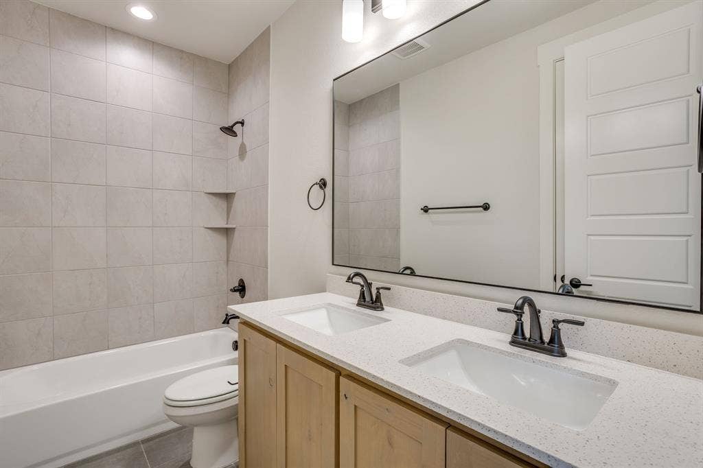 501 Olson Road, Waxahachie, TX 75167 Double vanity with light wood cabinetry, white stone-finish countertops, undermount rectangular sinks, large frameless mirror, and matte black fixtures throughout
