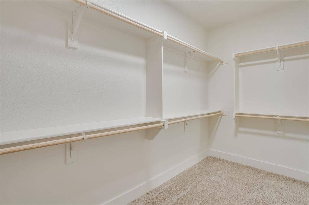 501 Olson Road, Waxahachie, TX 75167 Storage area featuring white built-in shelving, wooden garment rods, and wall-to-wall carpeting
