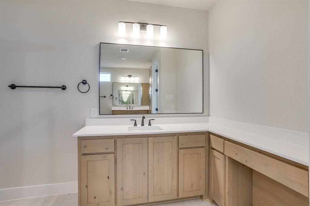 501 Olson Road, Waxahachie, TX 75167 Wood-finish cabinetry featuring an extended vanity counter, a rectangular integrated sink, a large framed mirror, and matte black hardware