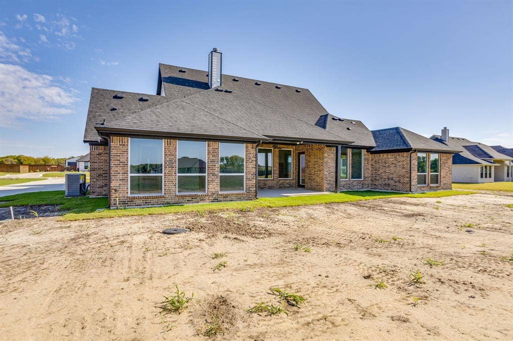 501 Olson Road, Waxahachie, TX 75167 Multi-faceted brick exterior featuring a shingle roof, chimney, expansive rear windows, and a covered patio