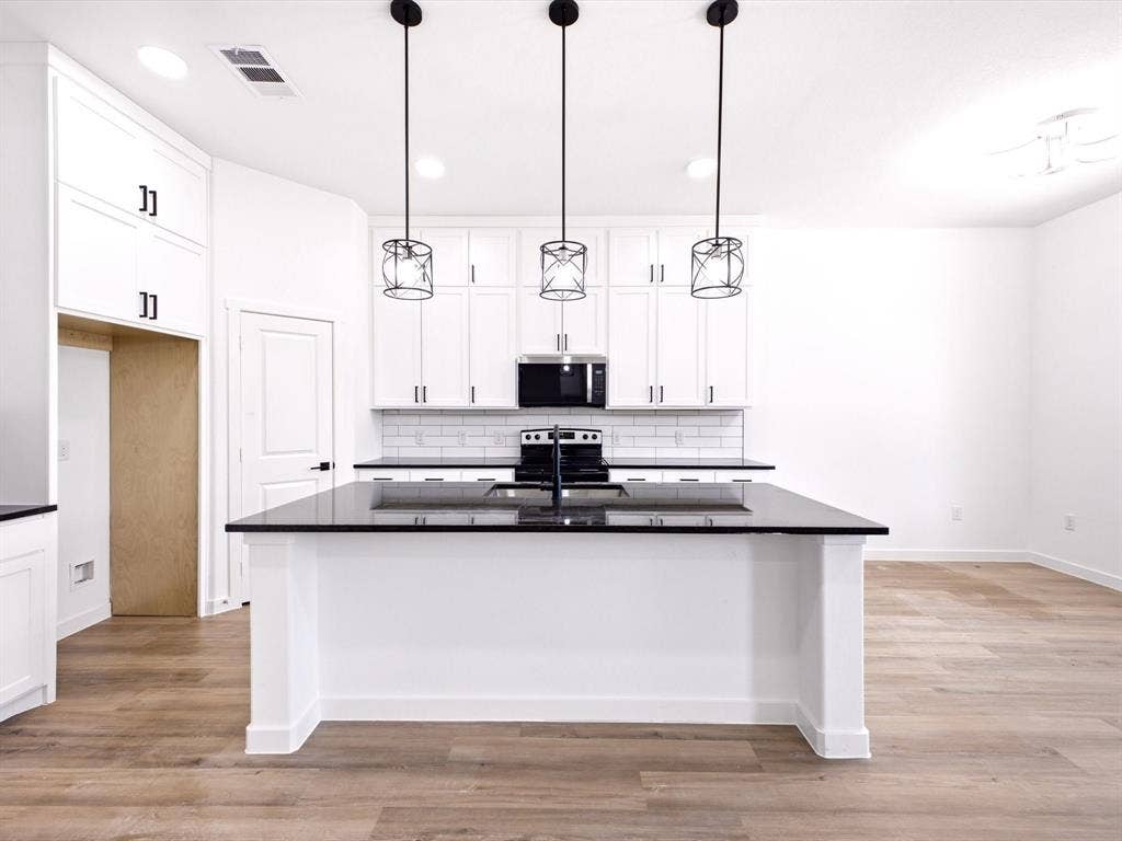 5365 Rabbit Trail, Kemp, TX 75143 Kitchen featuring white shaker-style cabinetry, a contrasting center island with a dark countertop, subway tile backsplash, and three black geometric pendant lights over a wood-finish floor