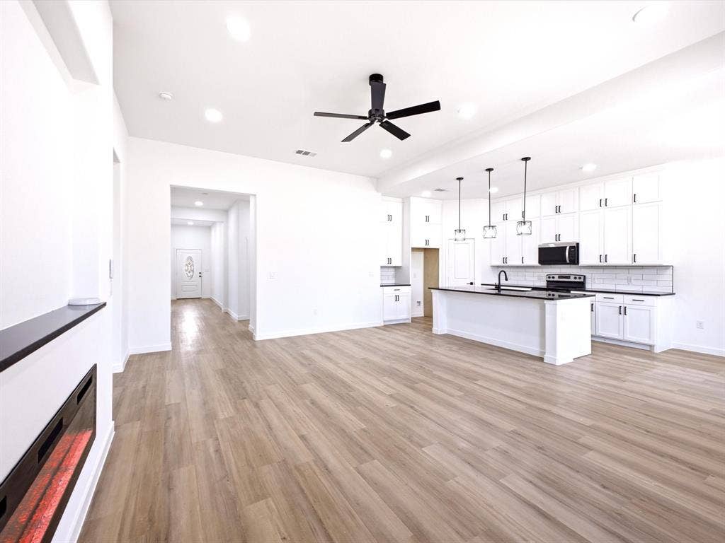 5365 Rabbit Trail, Kemp, TX 75143 Open-concept interior featuring wood-finish flooring, white cabinetry, a center island with a dark countertop, recessed lighting, and a built-in electric fireplace