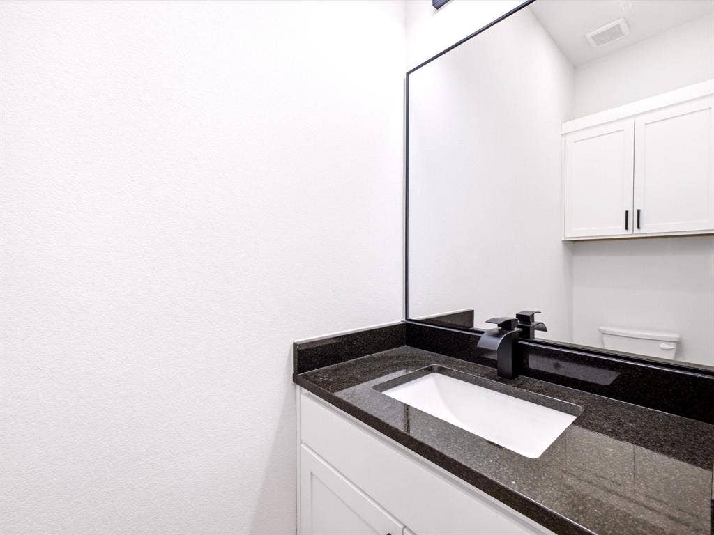 5365 Rabbit Trail, Kemp, TX 75143 Vanity featuring a dark stone countertop, integrated rectangular sink, matte black faucet, full-width mirror, and white shaker-style cabinetry with overhead storage