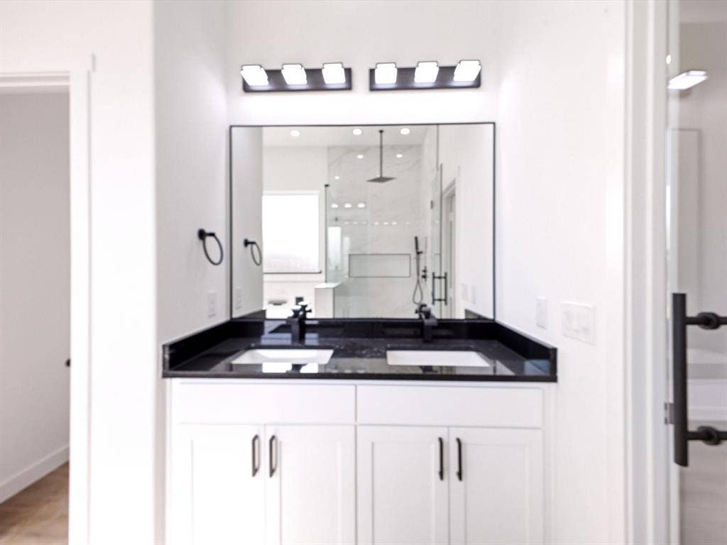 5365 Rabbit Trail, Kemp, TX 75143 Double vanity featuring white shaker-style cabinetry, dark countertop with dual rectangular undermount sinks, matte black wall-mounted fixtures, and a large frameless mirror with dual modern vanity lights