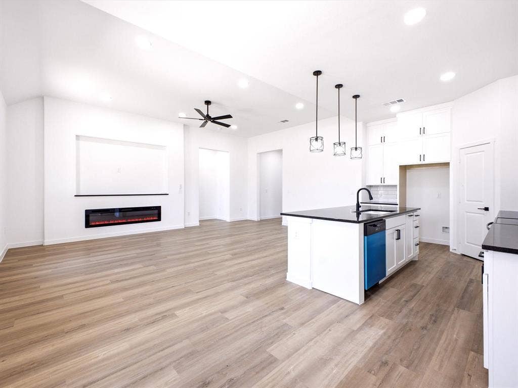 5365 Rabbit Trail, Kemp, TX 75143 Open-concept interior featuring wood-finish flooring, a wall-mounted electric fireplace, a kitchen island with stone-surface countertops, recessed lighting, and pendant fixtures