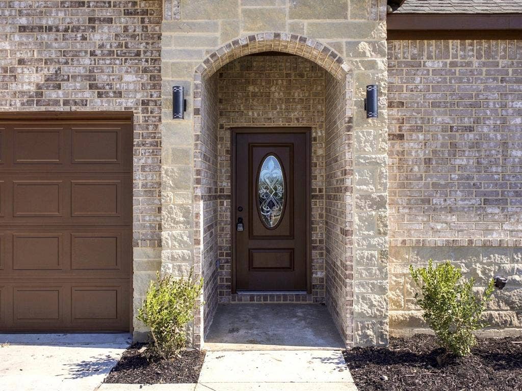 5365 Rabbit Trail, Kemp, TX 75143 Brick and stone masonry facade featuring an arched entryway, recessed front door with an oval glass inlay, and dual wall-mounted exterior light fixtures