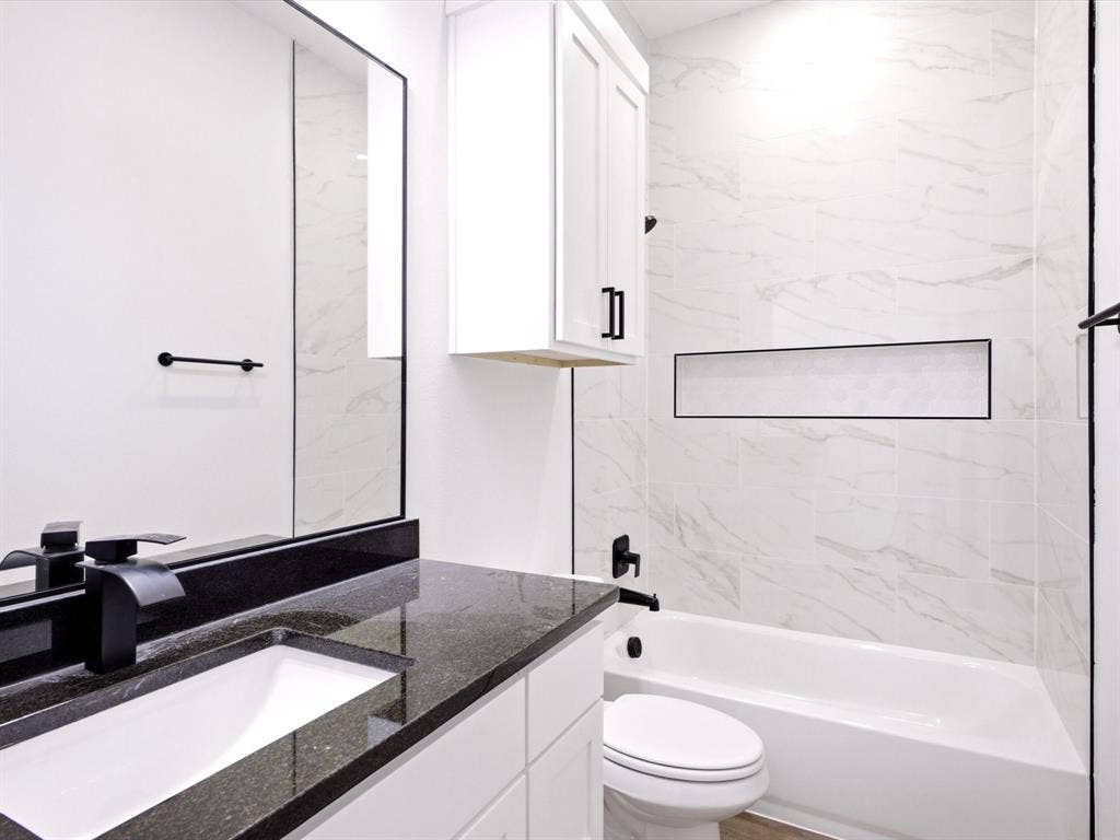 5365 Rabbit Trail, Kemp, TX 75143 White vanity with dark stone-finish countertop and undermount sink, complemented by a matte black faucet, wall-mounted cabinet, and shower area featuring large-format stone-finish tile surround with integrated recessed shelving