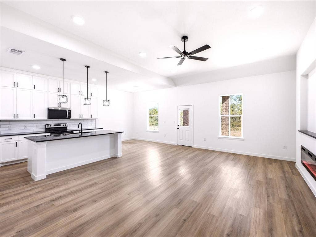 5365 Rabbit Trail, Kemp, TX 75143 Open-concept kitchen featuring white shaker-style cabinetry, dark stone-finish countertops, a central island with pendant lighting, wood-finish flooring, and a built-in linear fireplace