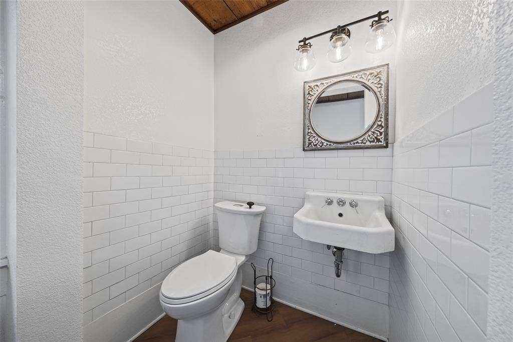 406 Summit Street, Farmersville, TX 75442 Wall-mounted porcelain sink, white subway tile wainscoting, wood-finish flooring, and three-light vanity fixture