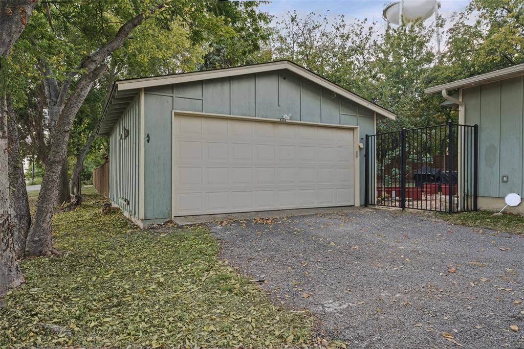 406 Summit Street, Farmersville, TX 75442 Detached two-car garage featuring vertical wood siding, a wide sectional garage door, gravel driveway, and a black metal perimeter fence