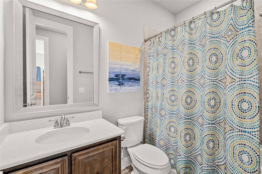 Bathroom featuring a vanity with wood-finish cabinetry, a white countertop, an integrated oval sink, a framed wall mirror, and a tub enclosure with tiled surround
