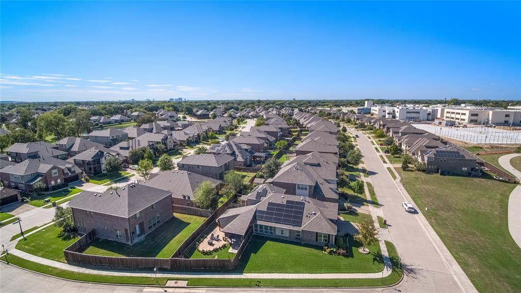 Aerial perspective of a multi-story residence featuring a brick facade, integrated solar panel array, attached garage, and a fenced rear yard with manicured landscaping