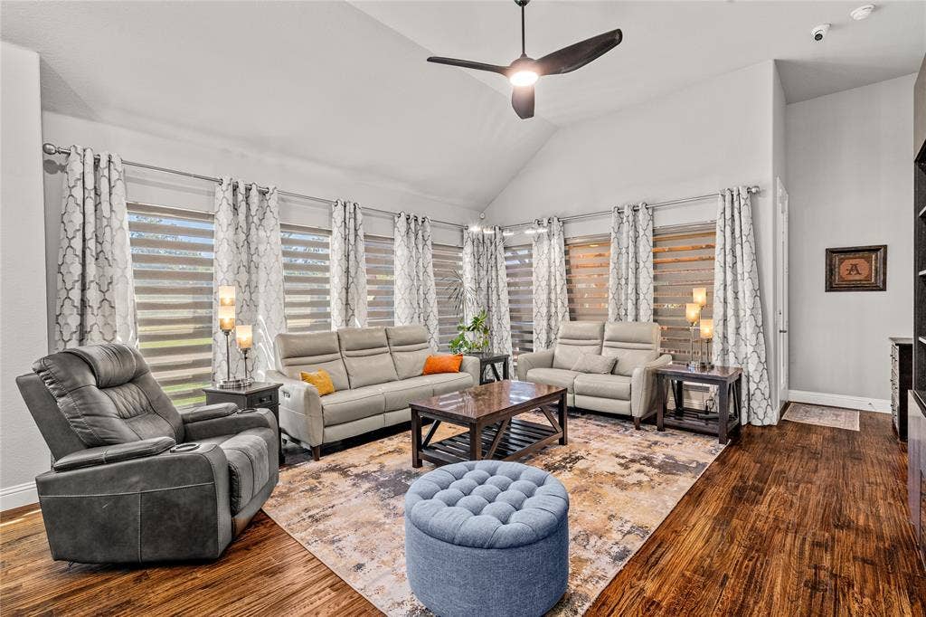 Vaulted ceiling featuring a central matte black ceiling fan, expansive windows with horizontal banded shades, and wood-finish flooring