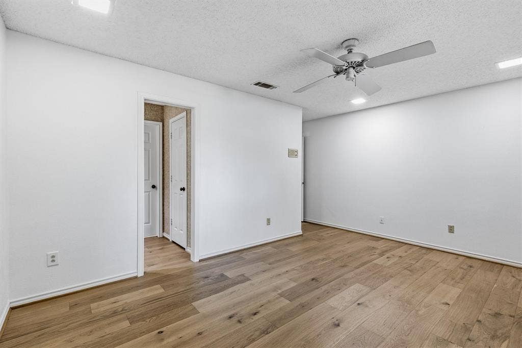 Wood-finish flooring, white walls, ceiling fan with light kit, and interior paneled doors
