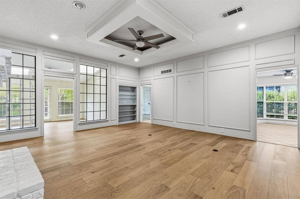 Architectural wainscoting, recessed tray ceiling with integrated ceiling fan, wood-finish flooring, grid-patterned windows, and built-in shelving