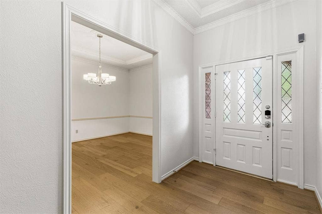 Foyer featuring wood-finish flooring, white paneled entry door with diamond-patterned glass inserts, matching sidelights, crown molding, and a multi-arm chandelier