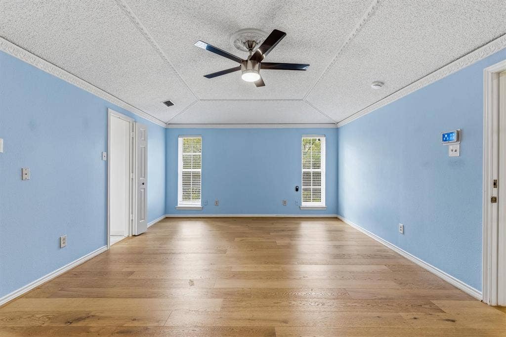 Room featuring wood-finish flooring, a tray ceiling with crown molding, and a central ceiling fan with an integrated light fixture