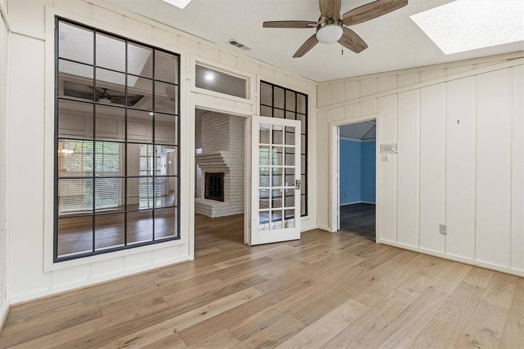 Board-and-batten wall paneling, wood-finish flooring, metal-framed glass partition, French door with grid-pane glass, and integrated skylights