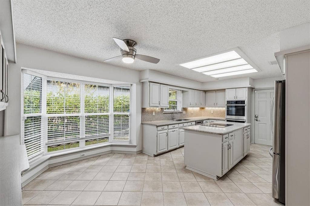 Kitchen featuring a central island with a stone-surface countertop, cabinetry with integrated under-cabinet lighting, built-in double ovens, recessed skylight, and bay windows