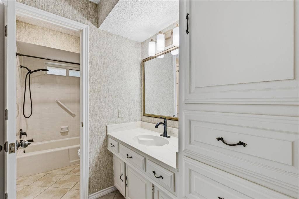 Bathroom featuring white cabinetry, a single-sink vanity with a solid-surface countertop, matte black fixtures, and a framed mirror