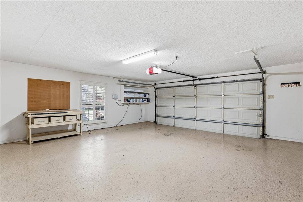 Attached oversized two-car garage featuring a sectional door, high-durability epoxy flooring, fluorescent overhead lighting, and a window with plantation-style shutters