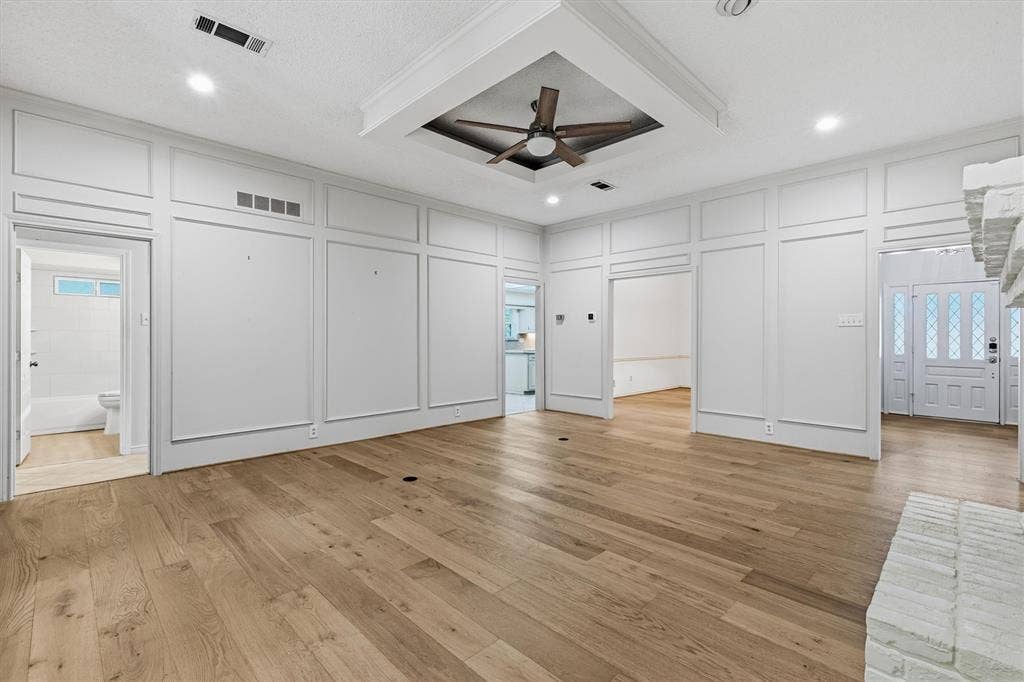 Spacious room featuring floor-to-ceiling wainscoting, wood-finish flooring, a tray ceiling with a recessed ceiling fan, and a white brick fireplace