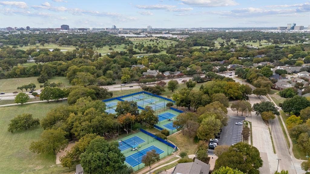 Aerial perspective of multiple fenced tennis courts, paved parking area, and mature landscaping