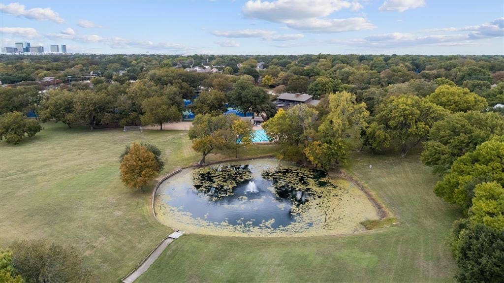 Aerial perspective featuring a natural pond with a central fountain, expansive manicured grounds, mature tree canopy, and an outdoor swimming pool