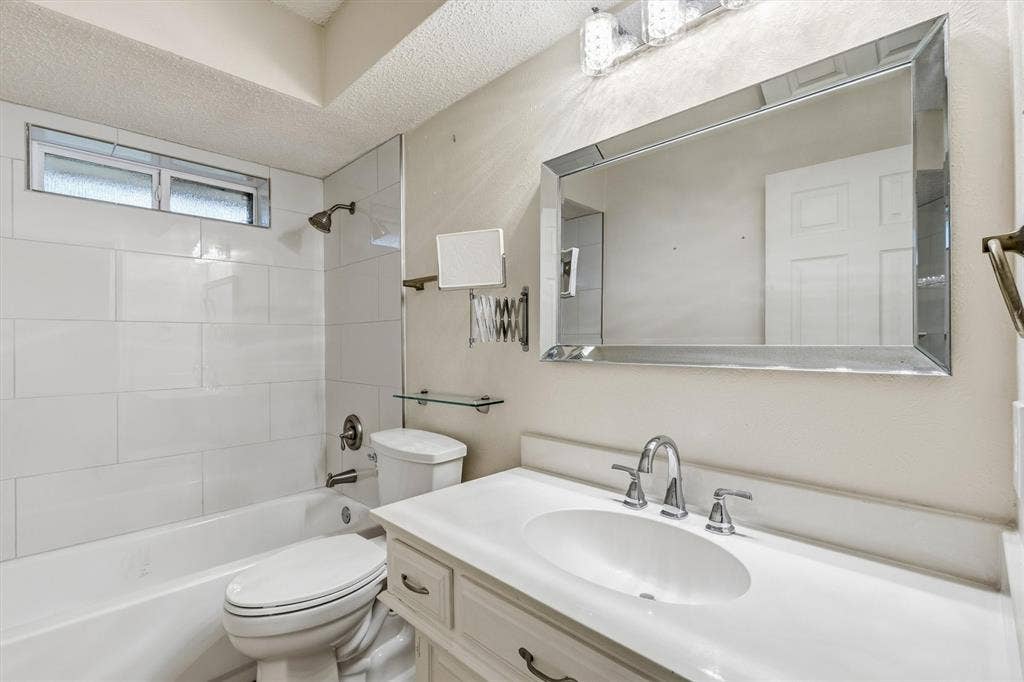 Bathroom featuring a white vanity with an integrated basin, beveled edge mirror, subway-tiled tub enclosure, and brushed metal fixtures
