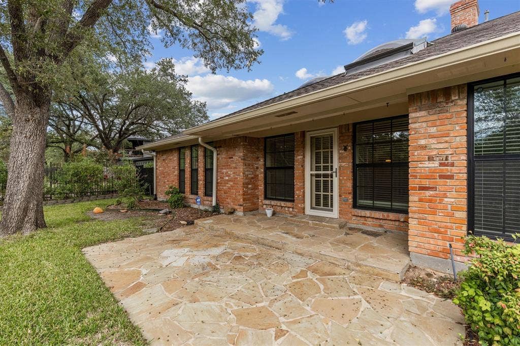 Exterior featuring a red brick facade, irregular flagstone patio, mature trees, and dark-frame windows