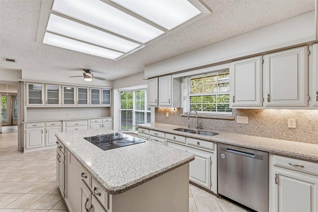 Kitchen featuring painted cabinetry, a central island with a built-in cooktop, stone-finish countertops, stainless steel dishwasher, and recessed ceiling lighting