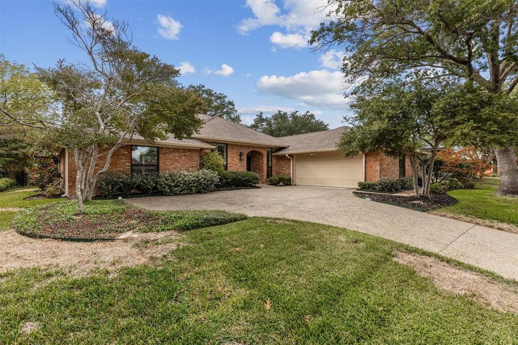 Single-story brick exterior featuring a multi-car attached garage, arched entryway, concrete driveway, and mature landscaping